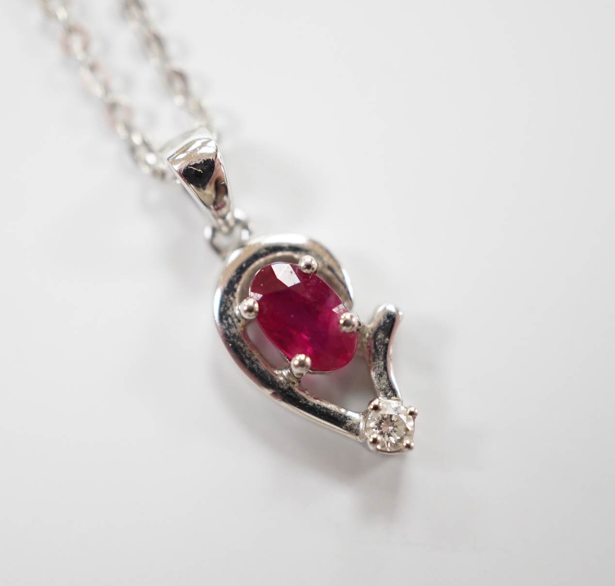 A modern 750 white metal, ruby and diamond set pendant, 9mm, on a 750 white metal chain, 42mm, gross weight 2.6 grams.